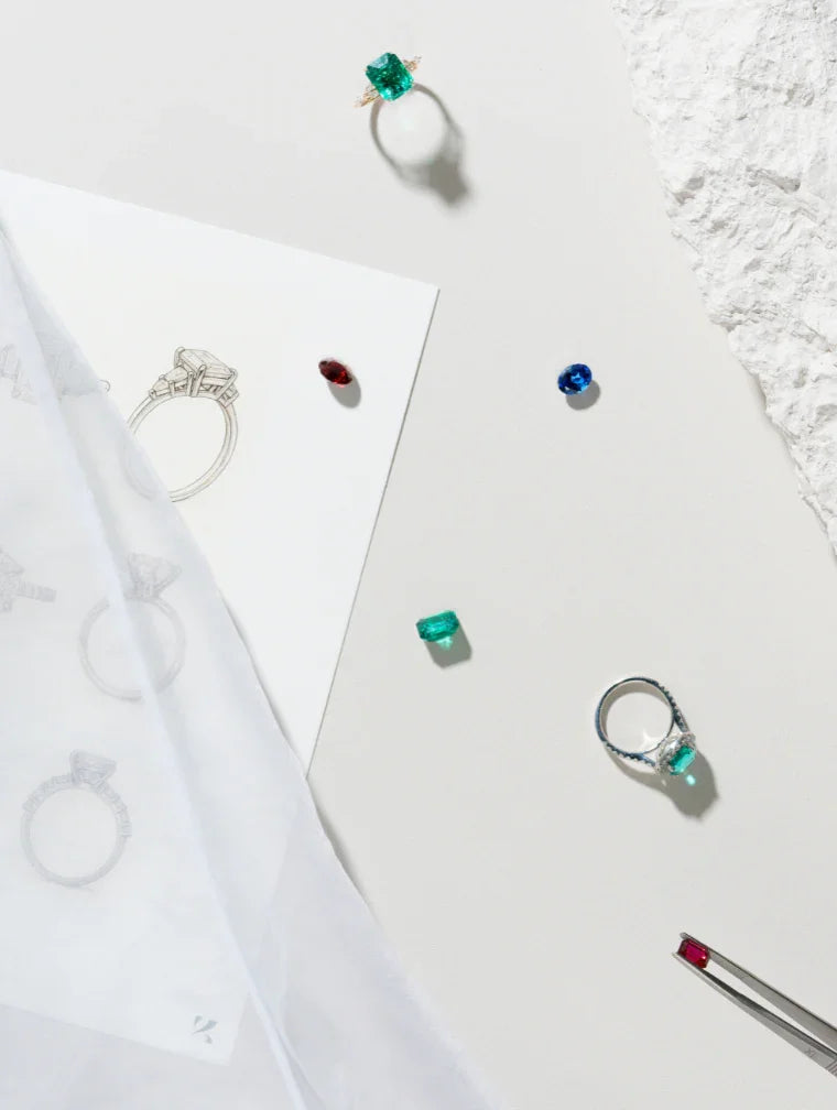 Keanis" jewelry design: Rings, emerald, ruby, sapphire gems, sketches, & tweezers on white.