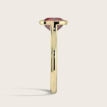 Side view of a lab-grown cushion ruby solitaire ring with a bezel setting in 18k yellow gold. "R25201CU.