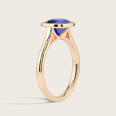 Lab-grown "cushion" cut sapphire solitaire ring in 18k rose gold bezel setting, side view.