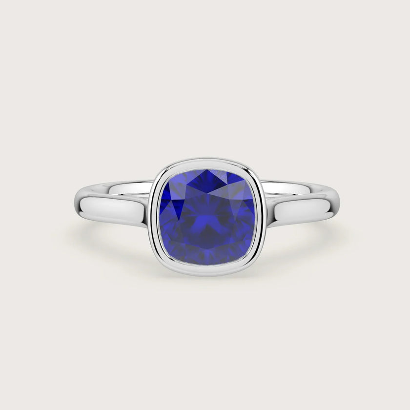 Lab-grown cushion sapphire solitaire "R25201CU" engagement ring in 18k white gold, bezel set.