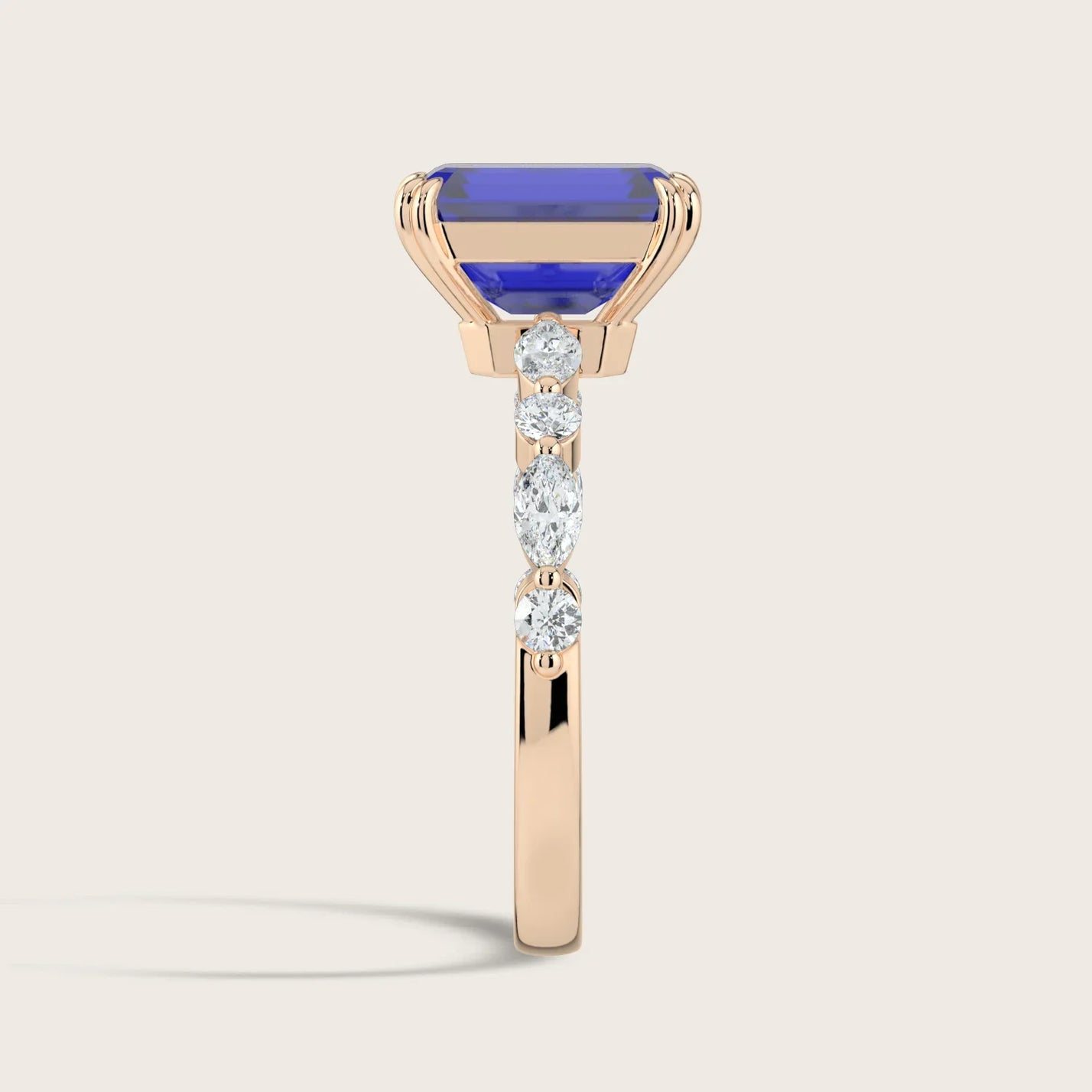 Rose gold ring with a lab-grown sapphire and diamond band. The sapphire is rectangular, and the diamonds are round and marqui
