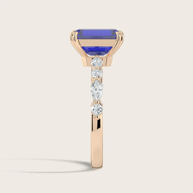 Rose gold ring with a lab-grown sapphire and diamond band. The sapphire is rectangular, and the diamonds are round and marqui