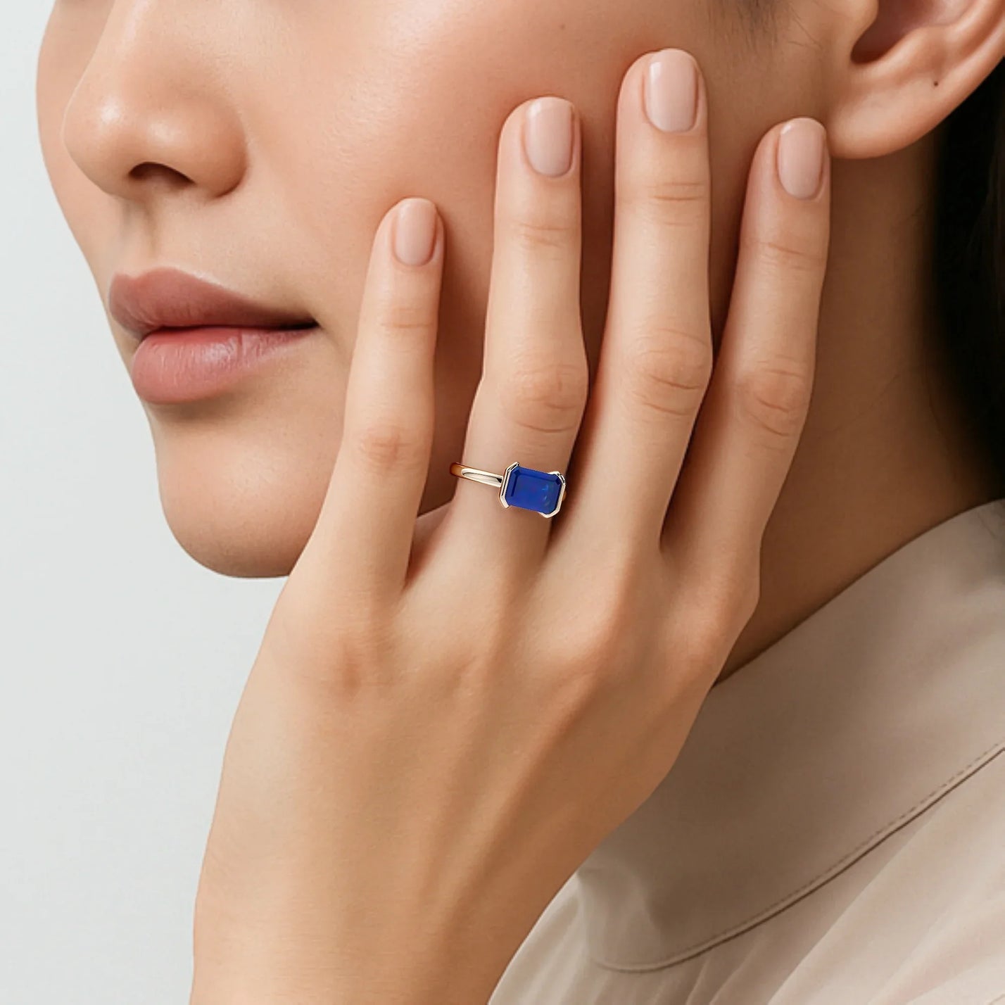 Woman wearing lab-grown "emerald-cut sapphire" solitaire ring in 18k rose gold half bezel setting.
