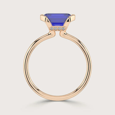 Lab-grown" sapphire ring. Emerald-cut blue stone in half-bezel setting with 18k rose gold band and small diamonds.