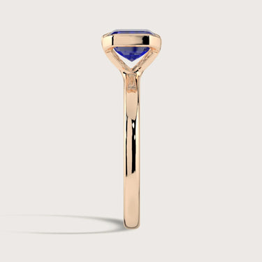 Side view of "R25201EM" lab-grown sapphire solitaire ring in 18k rose gold, half bezel setting.