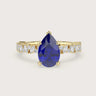 18k yellow gold engagement ring featuring a pear-shaped "lab-grown sapphire" and diamond band.