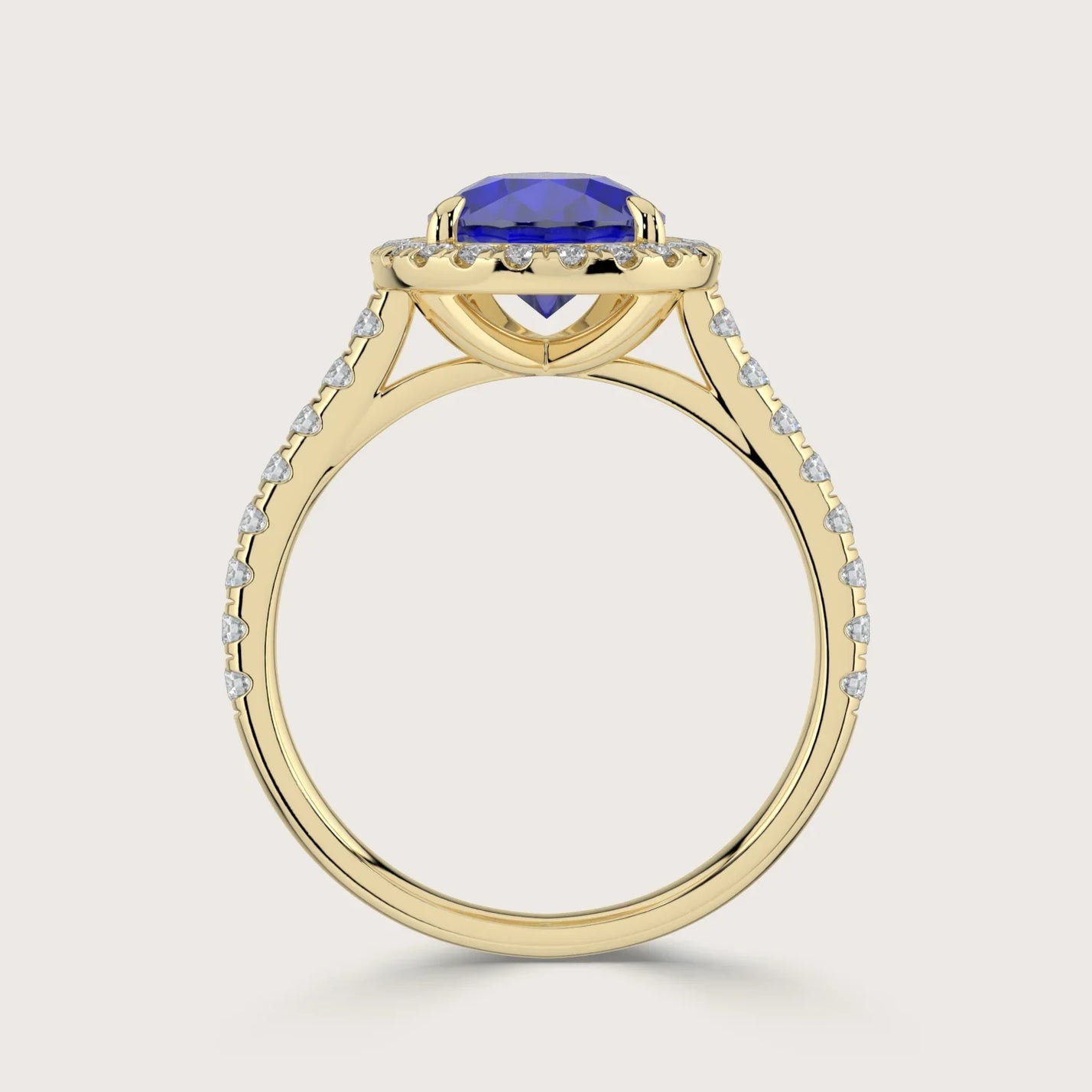 Close-up of a "lab-grown pear sapphire" ring with diamond halo and band in 18k yellow gold.