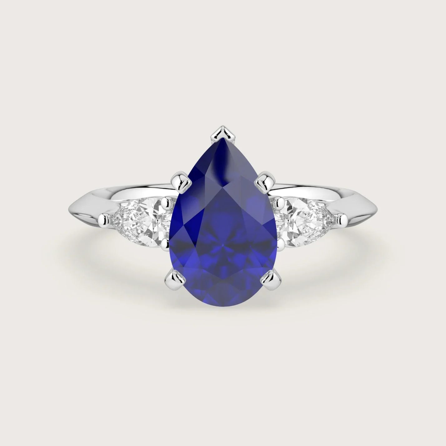 Lab-grown pear sapphire trilogy engagement ring. 18k white gold band, blue gemstone center, white side stones.