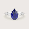 Lab-grown pear sapphire trilogy engagement ring. 18k white gold band, blue gemstone center, white side stones.